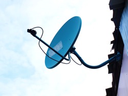 Blue satellite TV dish: Blue digital TV receiver installed next to the wall of the house or building. On the background of the blue sky with white clouds With copy space
