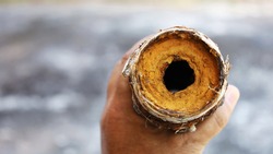 Man's hand holds a clogged metal pipe. Old water pipes had rusty slag and clogged dirt inside the pipe. On the background of a cement floor with a copy area. Close focus and select an object
