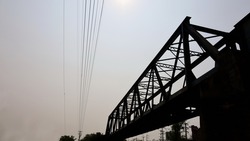 Silhouette of railway bridge. The iron bridge across the river on the background is cable and the sky with the afternoon sun shining with copy space. Selective focus