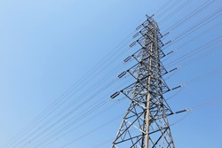 High voltage transmission lines on metal towers. Tall steel pylon structure with multiple high voltage power lines on blue sky background in bottom view with copy space and selective focus.