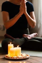 Close-up. Woman in yoga lotus pose meditating in a dark room with candle light. Atmosphere of relax and zen. Exercise to reach clarity of mind and perfect body. Wooden floor, soft morning light