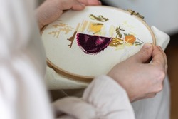 Cross-stitch embroidering in progress. Young girl in linen clothes is doing handmade embroidery. High quality photo