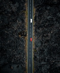 Vertical photo of the road with two cars with motion blur from above by drone - night time photo in Lanzarote. Straight road among the lavas on the sides in Canary Islands - dark moody shot.
