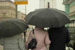 Family with black umbrellas. People rain. Parents with their daughter walk around the city. Bad weather on the street.