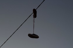 Sneakers hang on wire. Shoes hang on shoelaces on electrical wire. Boots against sky. Symbol of protest and mafia throwing shoes up on wire.