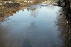 Big puddle in road. Water on asphalt. Road in park. Spring water spill.