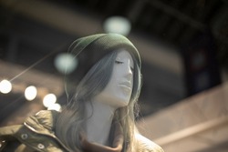 Mannequin of clothing. Girl in hat. Plastic figure of person. Details of shop window in clothes. Face of girl with long hair.