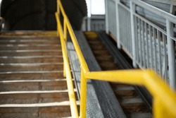 Steep stairs. Yellow handrail for climbing stairs. Overhead road crossing. Handrail for convenience.