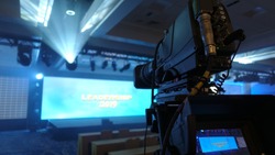 Professional video camera with long lens set up to shoot a corporate event, fog creates dramatic lighting effects                               