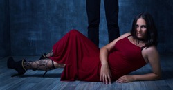 Book cover concept. Love couple Dominance and submission. Woman lay on the floor in red dress with hose