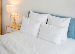 White pillows, duvet and duvet case on a blue bed. White bed linen on a blue sofa. Bedroom with bed and bedding. Right side view.