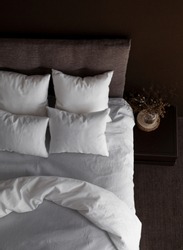 White pillows, duvet and duvet case on a bed with brown headboard. White bed linen on the sofa. Bedroom with bed, white bedding, nice posy on the bedside and black wall. Top view.