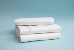 Stack of white bedding against blue backdrop, folded soft bed clothes, stack of white cotton sheets on a blue background for advertising, commercial and mock up