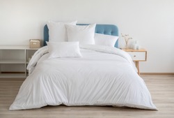 Interior with white bed linen on the sofa. Bedroom with bed, white bedding, and bedside table. White pillows, duvet and duvet case on bed with blue headboard. Front view.