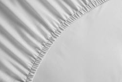 Bed corner with white fitted sheet. White sheet with elastic band. Bed cover close up photo.