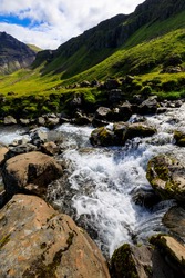 Blurred motion of water flowing over rapids in the fast flowing Grundara River, with a backdrop of green mountain cliffs, Summer, Grundarfjordur,  Snaefellsnes Peninsula, West Iceland, Europe