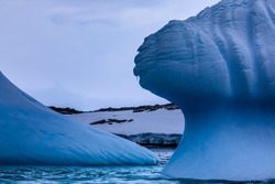 Amazing Antarctic scenery with icicles hanging from the sculptural shaped and weathered blue ice of a melting blue iceberg from an Antarctic glacier floating in the icy blue sea of coastal Antarctica