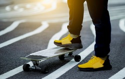 Young man's legs in sneakers on skateboard with sunset, Blurred background.