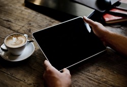 hands of a man holding blank tablet device over a wooden workspace table
