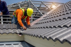 Roof repair, worker  replacing gray tiles or shingles on house with blue sky as background and copy space, Roofing - construction worker standing on a roof covering it with tiles.