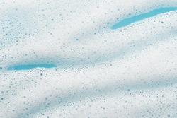 Foam lather texture. White cleanser gel, shaving foam, shampoo bubbles on blue background. Foamy skincare cosmetic product