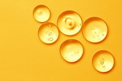 Vitamin serum oil texture. Orange skincare gel drops on color background. Gold cosmetic liquid product close up