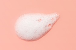 Skincare cleanser foam texture. Soap, shampoo, cleansing mousse bubbles swatch on pink color background. Face wash lather closeup