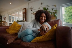 Portrait of black woman playing with pet dachshund dog at home sitting on couch