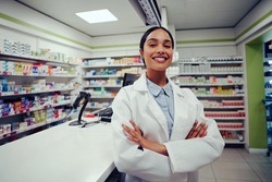 Proud young female with folded hands in labcoat standing in chemist near counter