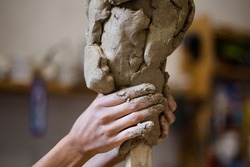 Female hands create a clay head sculpture in art studio
