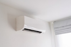 Air conditioner on white concrete wall in area of bedroom space.