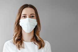 Portrait of a young woman in a medical mask isolated over grey background. Young girl patient stands against the wall background, copy space for text