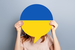 Student girl holds blank white speech bubble with Ukrainian flag isolated over grey studio background. woman holding a round information piece of paper dialog.