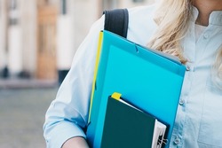 female student holding a folder and a notebook in her hands on a university background. Girl is taking exams at university