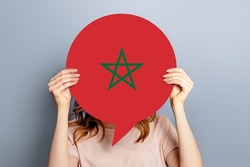 student girl holds blank white speech bubble with the flag of Morocco isolated over grey studio background. woman holding a round information piece of paper dialog