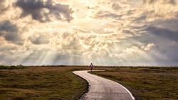 A person walking alone along s-shape path. The sun produces amazing light rays across the sky. The image is simple and breathtaking. This image is suitable for background use or add quote above.