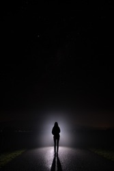Silhouette of a woman in the darkness. Night Photography. Bright light shining behind dark mysterious figure. Ghostly, mystical, surreal person standing.
