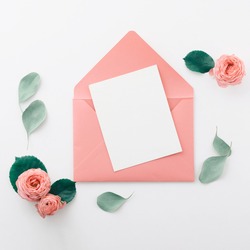 Flat lay shot of letter and envelope on white background. Wedding invitation cards or love letter with pink roses. Valentine's day or mother day holiday concept, top view, flat lay, overhead view
