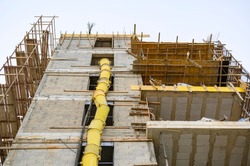 The process of building a residential building. Scaffolding, yellow chute, safe waste disposal. Open facade. View from below. Horizontal view. Urban view.