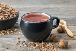 Herbal tea cup, healthy oak bark in black ceramic bowl and acorns on wooden table. Herbal medicine. 
