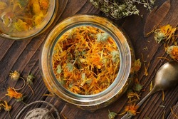 Glass jar of dried calendula flowers, cup of healthy calendula herbal tea, thyme medicinal herbs on wooden table. Top view. Alternative herbal medicine.