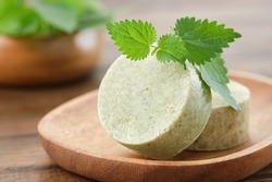 Nettle solid shampoo pieces or homemade natural organic soap bars, fresh green nettle leaves. Selective focus.