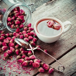 Dry rose flowers, tea cup, strainer and glass jar with rose buds. Selective focus. Retro styled photo.