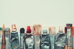 Row of artist paintbrushes and paint tubes closeup on artistic canvas background, retro stylized. Copy space for text.