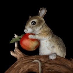 Cute little mouse with red apple isolated on a black background. antique porcelain figurine of a mouse