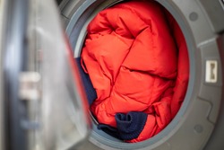 Open door in washing machine with dirty down jacket inside, close up, preparation for cleaning, copy space