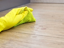 Hand in yellow rubber protective glove cleaning dirty filthy floor with micro fiber cloth from dust indoors, copy space, horizontal