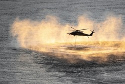 Up close shot of helicopter performing training rescue operation over the columbia river at sunset. Water splashes, vapor and sprays rise from the river surface. Rope hangs from the helicopter.