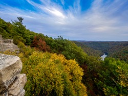 View from the top of Cooper’s Rock in Coopers Rock State Forest in West Virginia right before sunset with the valley of fall colored trees below, the water running through and a beautiful blue sky