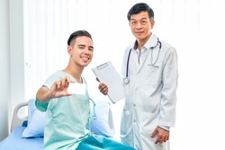 Happy Caucasian man patient holding mock up blank white card on hospital bed while Asian doctor standing,healthcare insurance card or credit card to pay for medical fee. healthcare insurance concept.